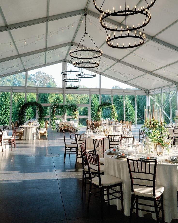 Elegant wedding reception at Venue By Choice banquet hall with glass walls, greenery arches, and classic round tables.