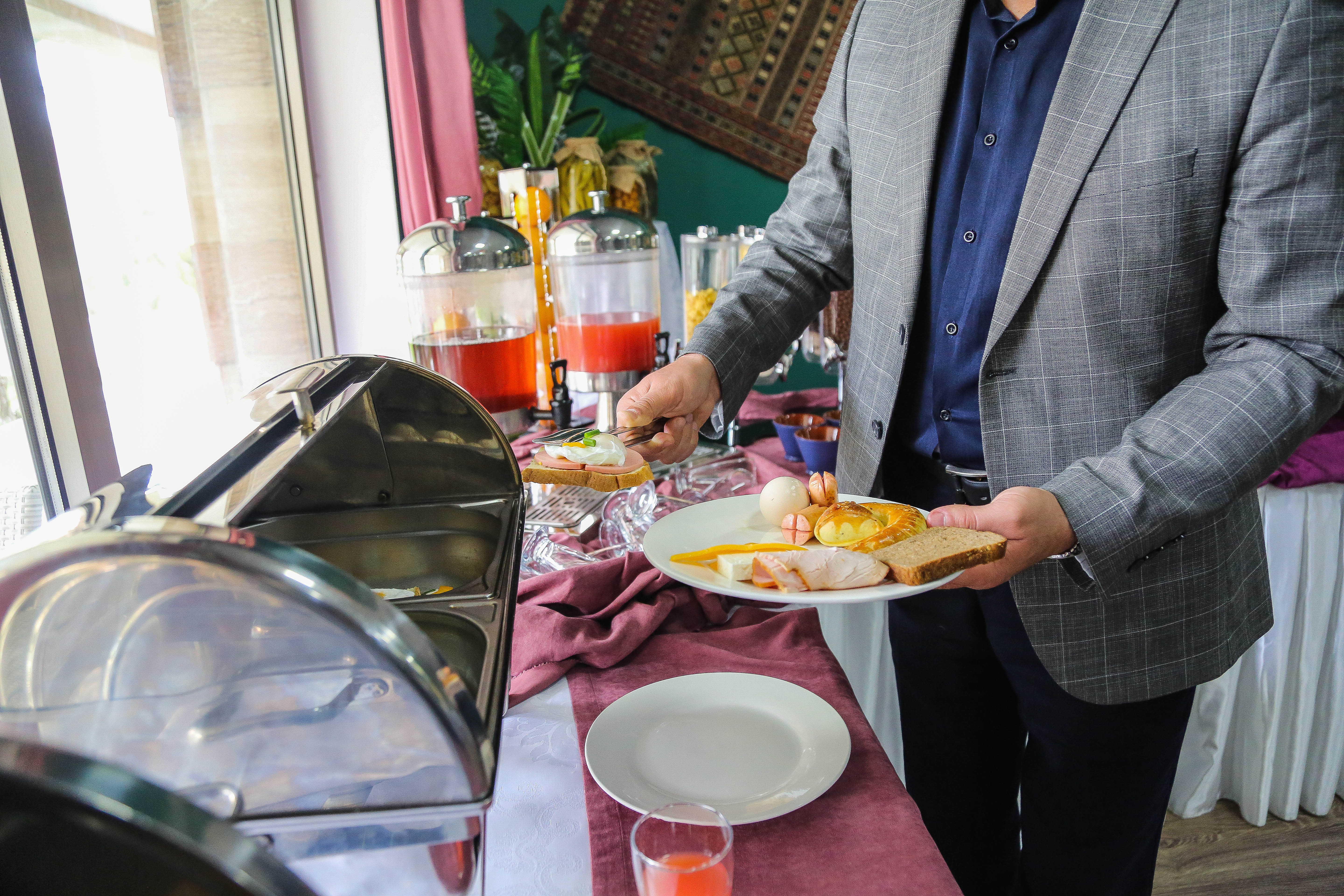 side view man lays breakfast food egg sausages bun toast and cheese on a plate from the open buffet in a party hall