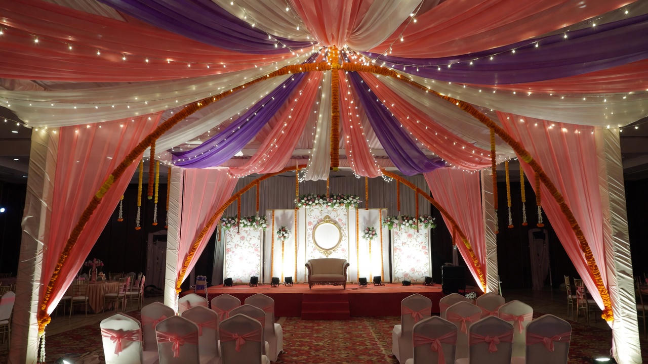 Low budget wedding stage decoration in Kolkata banquet hall with pastel drapes, fairy lights and marigold garlands"